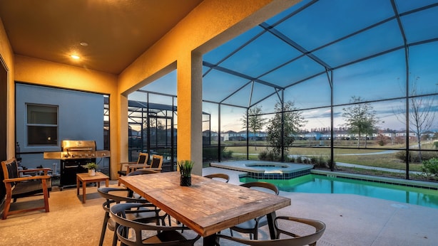 Une terrasse avec une table et des chaises en bois, un barbecue et une vue sur une piscine et un paysage verdoyant.