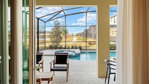 Une terrasse fermée par des baies vitrées, avec une piscine, des chaises et une vue sur un quartier résidentiel.
