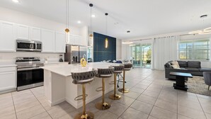 Une cuisine moderne avec des meubles blancs, des appareils en acier inoxydable et un îlot central doté de tabourets de bar.