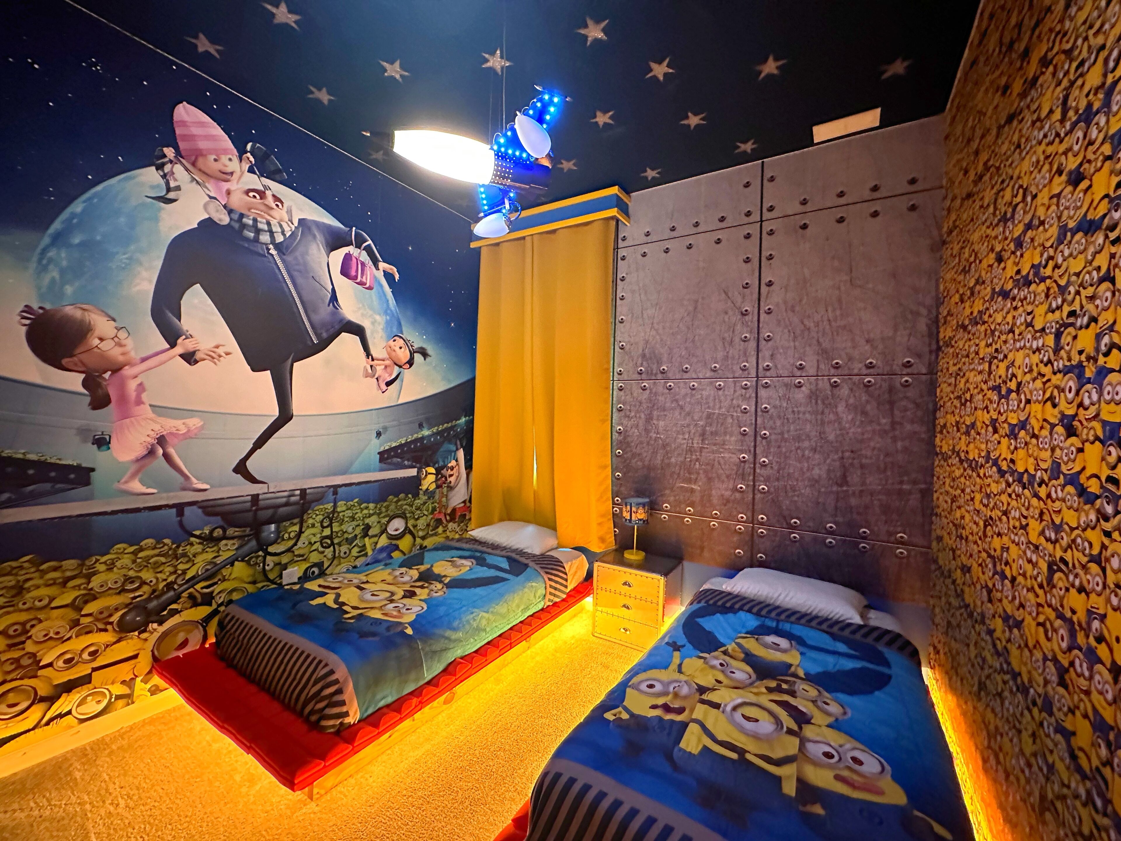 A children's room with a Minion-themed bedspread, a mural of a character on the wall, and a starry night ceiling.