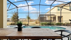 Un espace piscine extérieur avec une table et des chaises en bois, entouré d’une structure en verre.