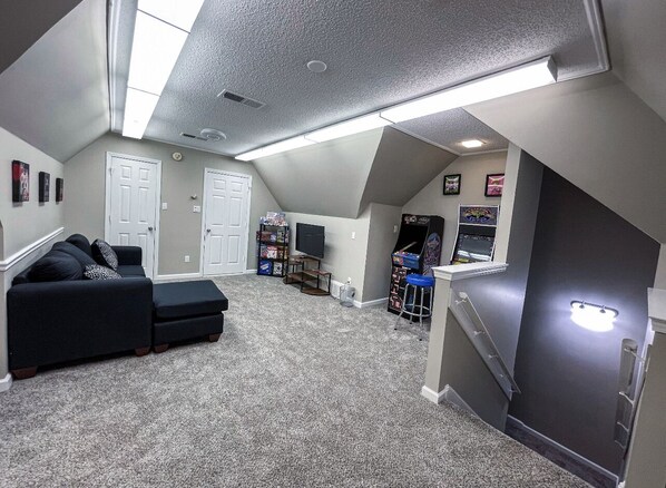 Una habitación amplia con un sofá modular negro grande, una mesita y una consola de videojuegos.