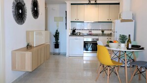 A modern kitchen with white cabinets, a built-in oven, and a dining area with a yellow chair and a small table. - 37C TB fantastic views (Calp)