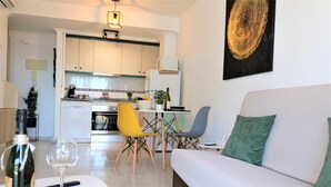 A modern living room with a white sofa, a dining table with chairs, and a kitchen in the background. - 37C TB fantastic views (Calp)