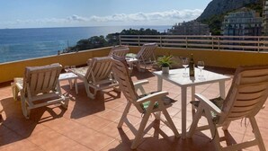 A terrace with white chairs and tables, overlooking a coastal view with buildings in the background. - 29D Spectacular views parking and wifi (Calp)