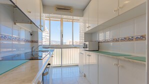 A kitchen with white cabinets, a microwave, and a view of the city through a large window. - 29D Spectacular views parking and wifi (Calp)