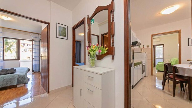 Ein Hotelzimmer mit einem Bett, einem Schminktisch, einem Spiegel, einer Vase mit Blumen, einem Essbereich mit Tisch und Stühlen sowie einer Küchenzeile mit Kühlschrank und Herd.