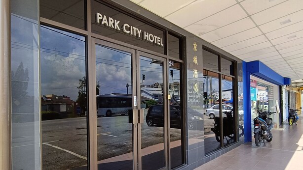 Exterior del Hotel Park City, con amplias puertas de vidrio, un felpudo rojo en la entrada y vista despejada de la calle.