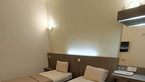 Habitación de hotel con dos camas individuales, una mesita de noche con lámpara y un escritorio pequeño con silla.