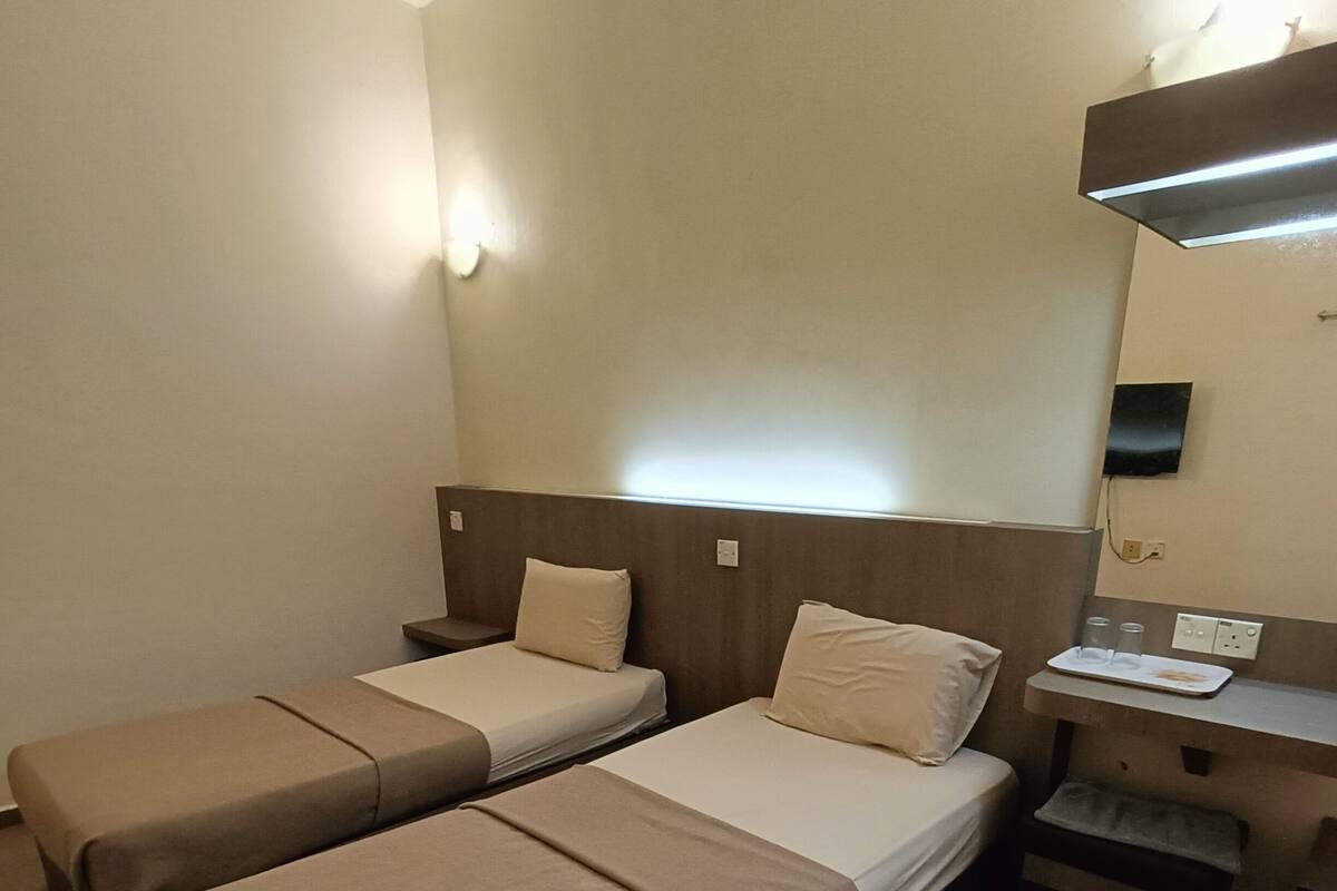 Habitación de hotel con dos camas individuales, una mesita de noche con lámpara y un escritorio pequeño con silla.
