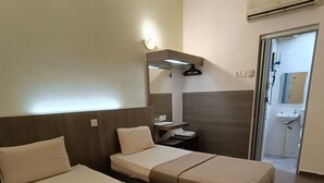 Habitación de hotel con dos camas, una mesita, un espejo y un baño visible a través de una puerta abierta.