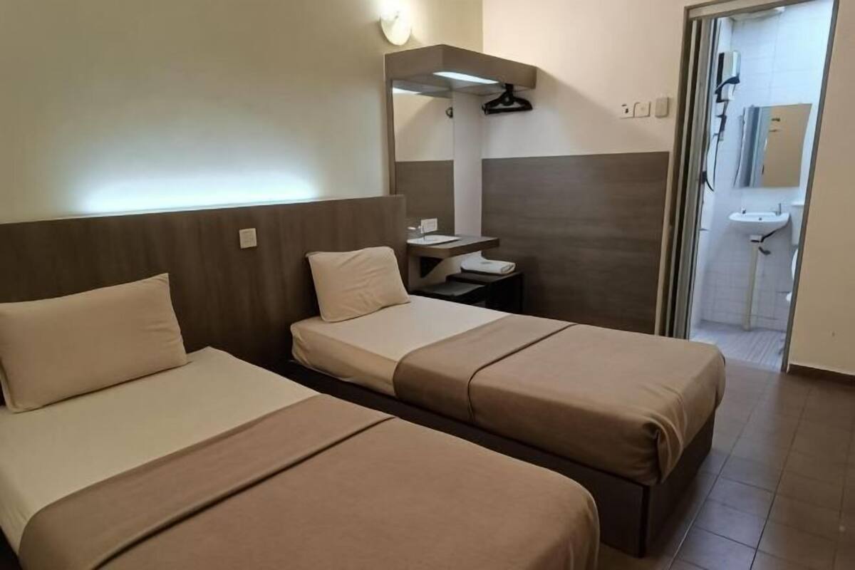 Habitación de hotel con dos camas, una mesita de noche pequeña, un espejo y un baño visible a través de una puerta abierta.