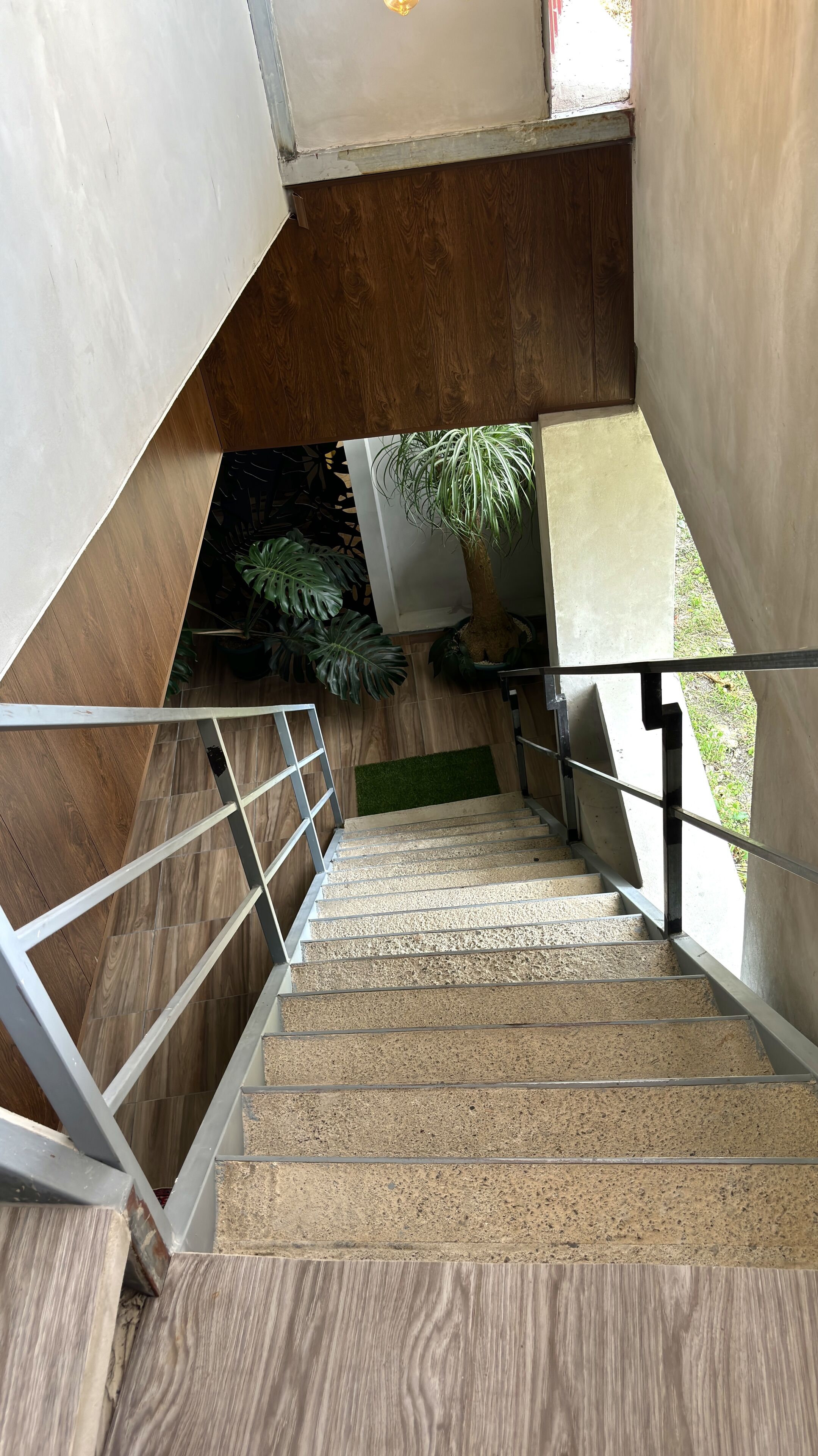 A staircase with a wooden finish, metal railings, and a view of a garden outside.