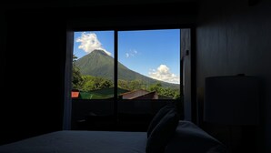 A hotel room with a bed, a window, and a view of a mountain. - Arenal Monara (La Fortuna)