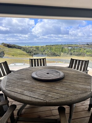 Mesa de madera redonda con un agujero central, rodeada por cuatro sillas, en un balcón con vista a un paisaje costero.