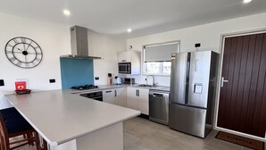 A modern kitchen with a central island, stainless steel appliances, and a large wall clock. - Karikari Vista (Karikari Peninsula)