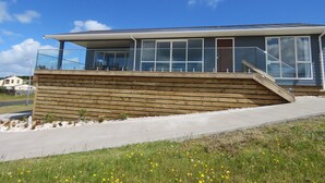 A modern building with a flat roof, large windows, and a wooden deck. - Karikari Vista (Karikari Peninsula)