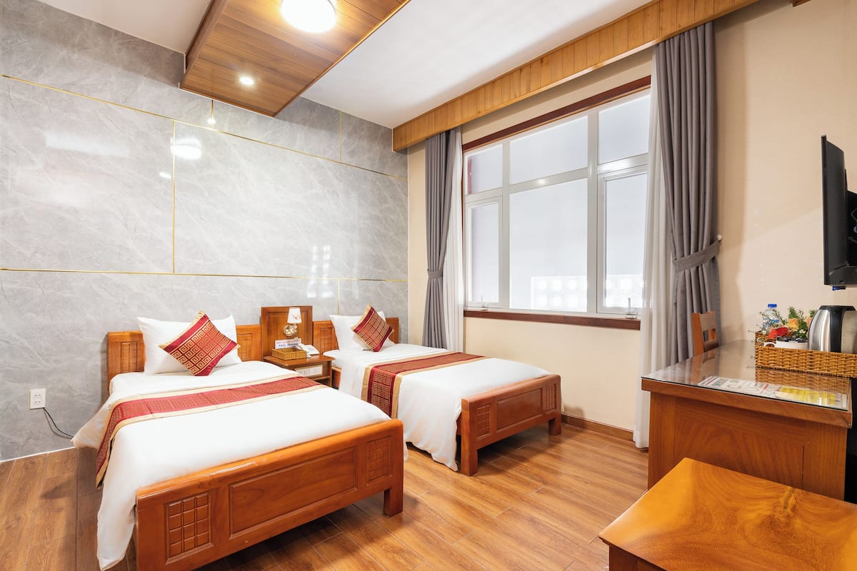 Habitación de hotel con dos camas de madera, un escritorio de madera, televisión y ventana con cortinas.