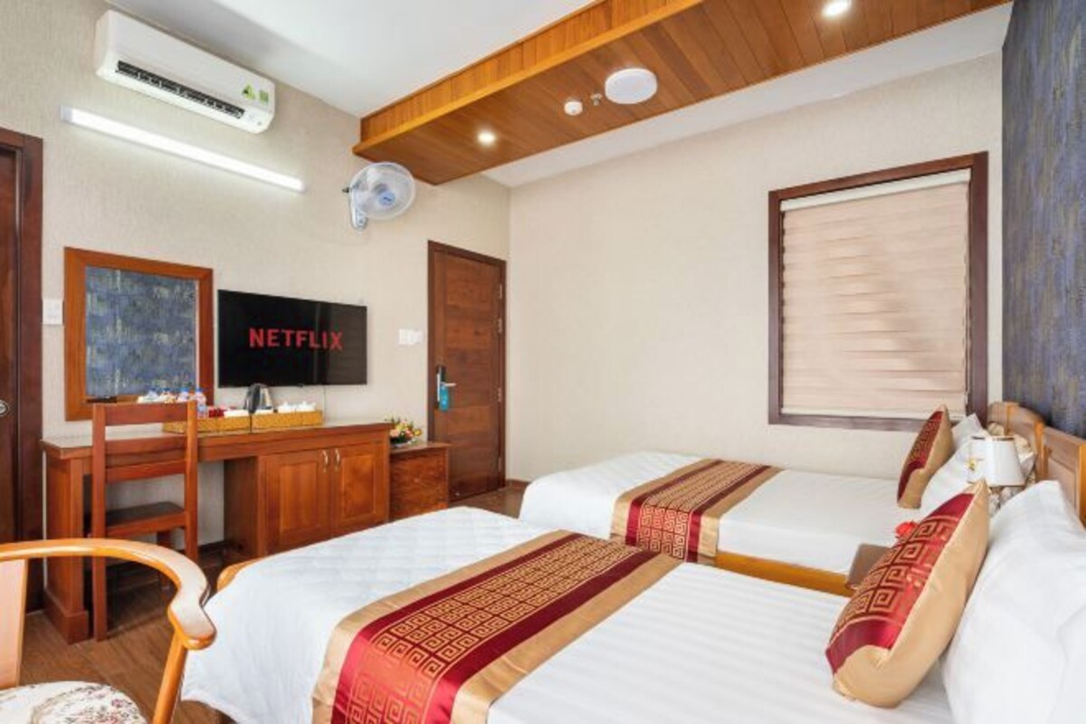 A hotel room with two beds, a desk, a television, and a window with blinds.