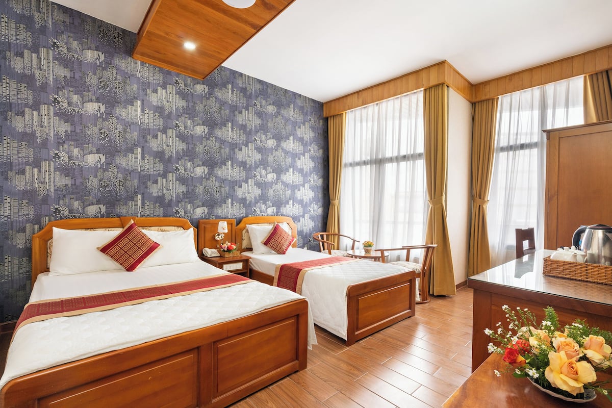 Habitación de hotel con dos camas de madera, un escritorio de madera, un espejo, una ventana con cortinas y una pared con diseño.