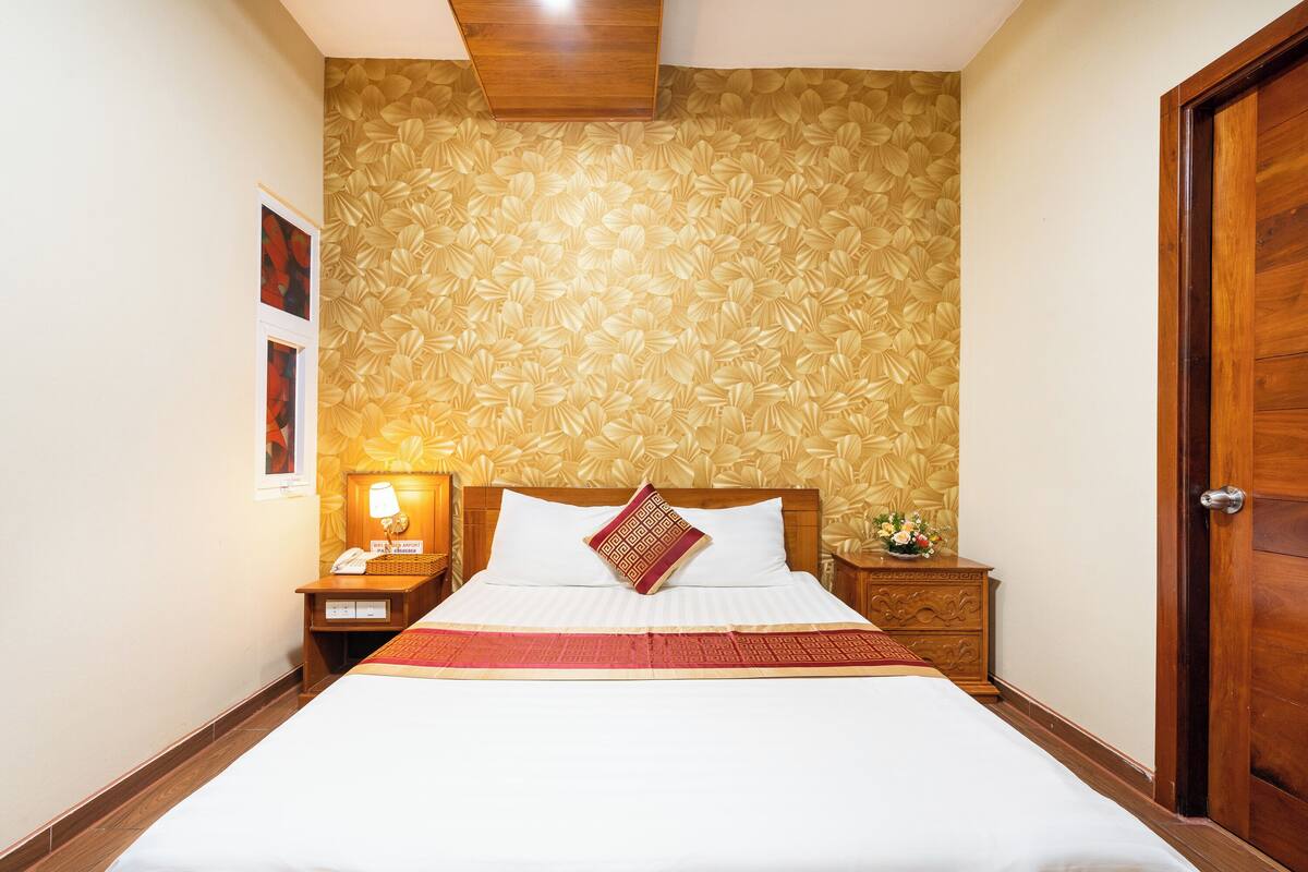 Una cama bien hecha con una colcha blanca y roja, un cabecero de madera y un estampado floral en el papel tapiz de la pared.