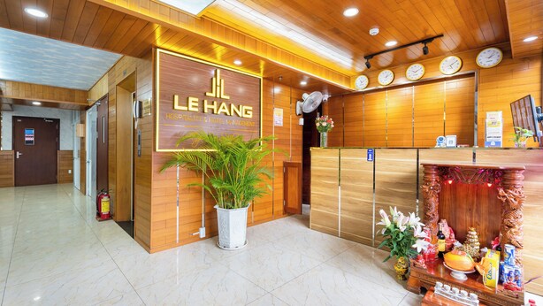 A hotel reception area with a wooden reception desk, a large sign for Le Hang Hospitality & Hotel Management, a fire extinguisher, and a potted plant. - Saigon Airport Hotel  (Ho Chi Minh City)