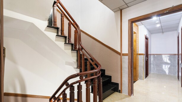 Eine Treppe mit hölzernen Geländern und schwarzen Stufen, die zu einem Raum mit Fliesenboden und einer Holztür führt.
