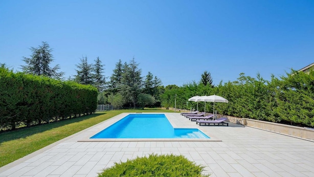A rectangular swimming pool with a tiled deck, surrounded by neatly trimmed hedges and trees. - Cozy home in Porec with WiFi (Porec)