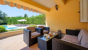 A balcony with wicker furniture, a table with cups and pastries, and a view of a swimming pool and greenery. - Cozy home in Porec with WiFi (Porec)