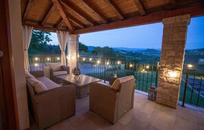 A covered outdoor seating area with wicker furniture, string lights, and a view of the landscape.