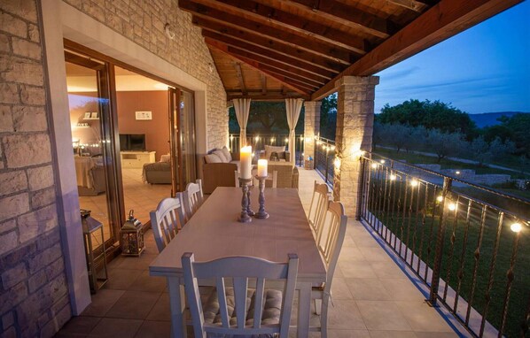 An outdoor patio with a dining table and chairs, a stone wall, and a view of the landscape.