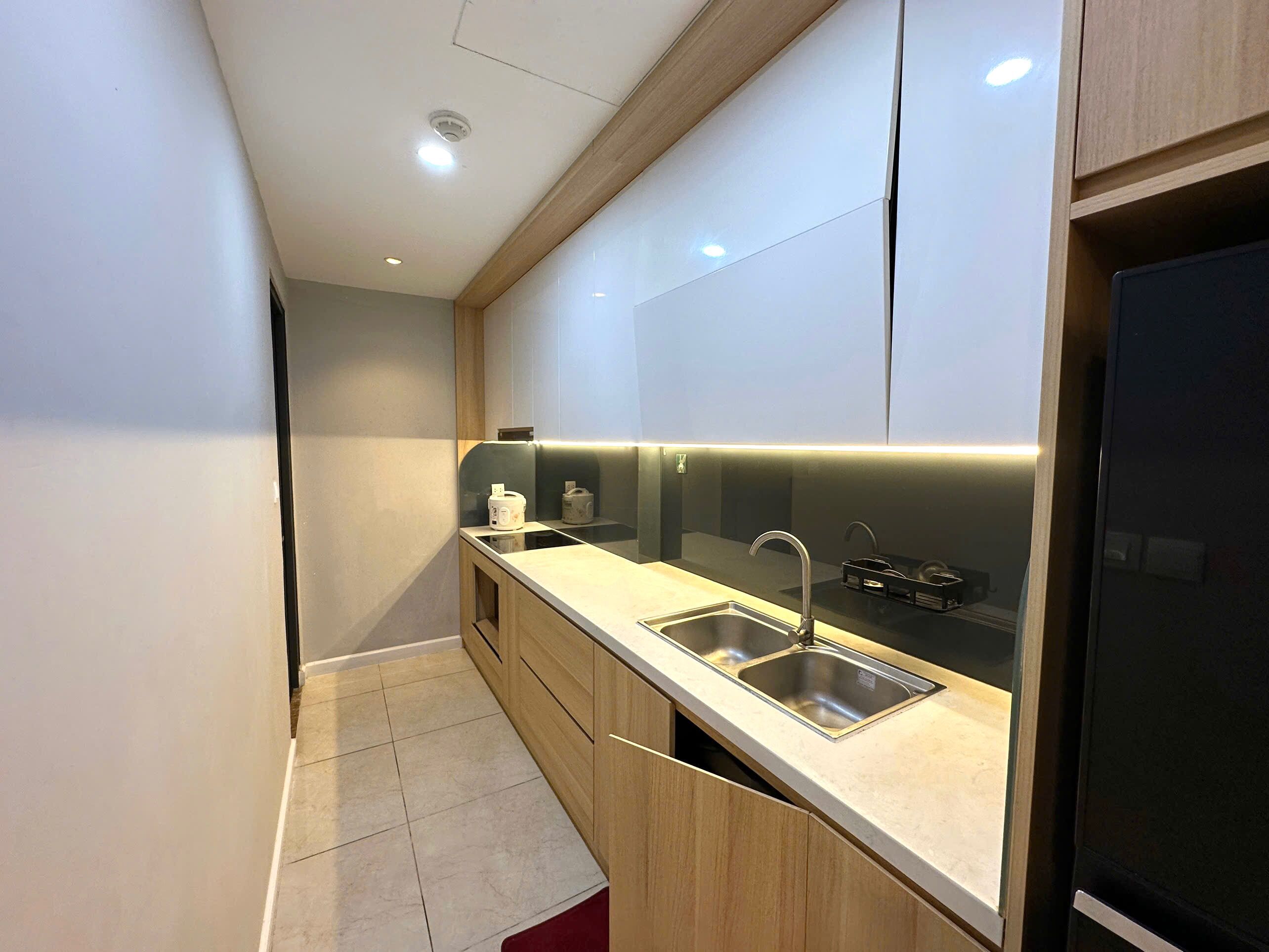 A modern kitchen with two sinks, wooden cabinets, and a black refrigerator.