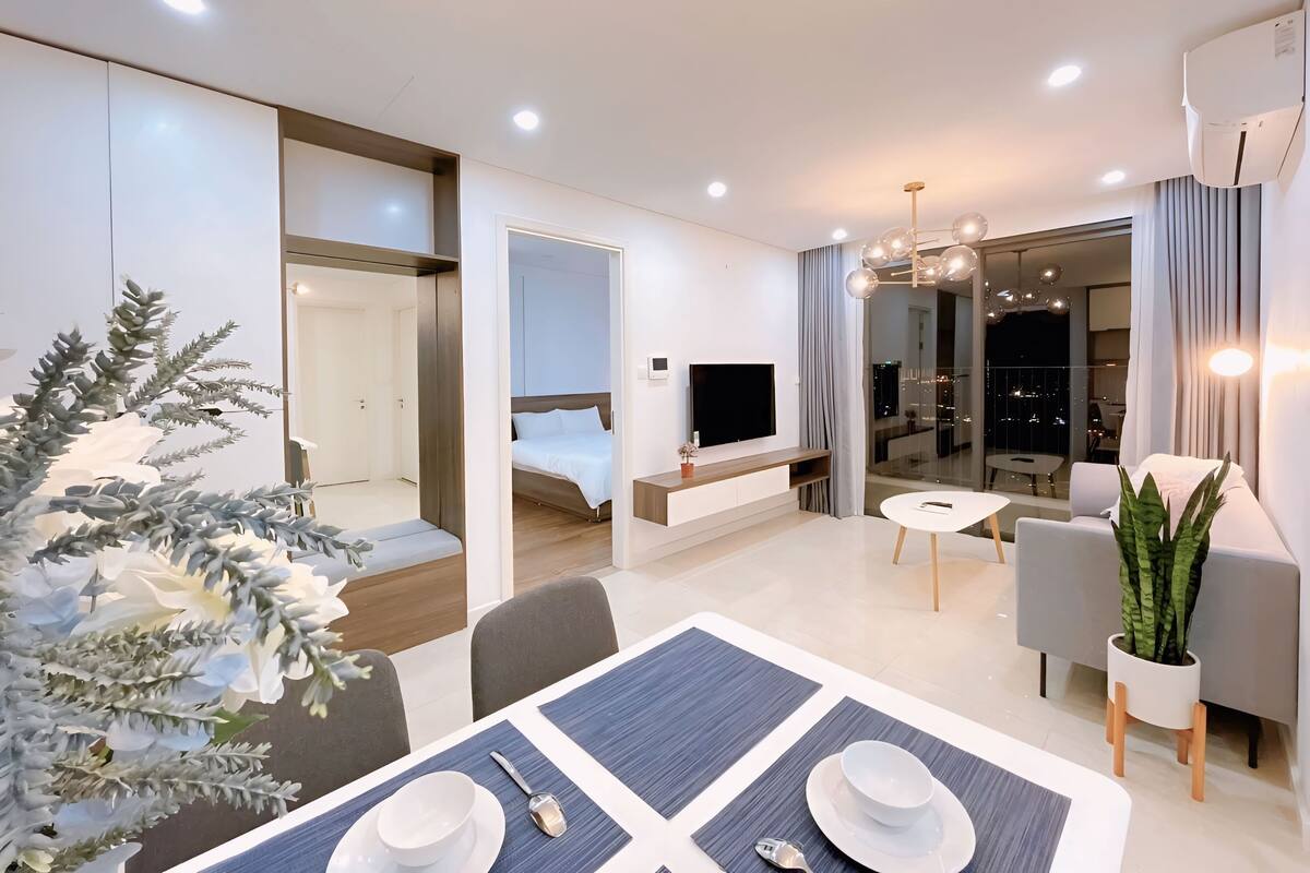 Une chambre d’hôtel moderne dotée d’un coin repas, d’une télévision, d’un balcon avec vue sur la ville et d’une grande plante en pot.
