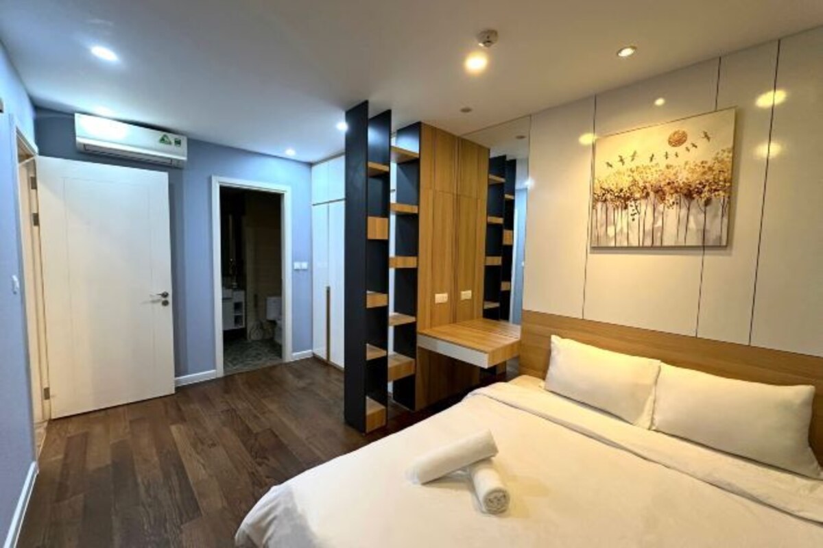 A modern bedroom with a large bed, built-in shelving, and a painting on the wall.