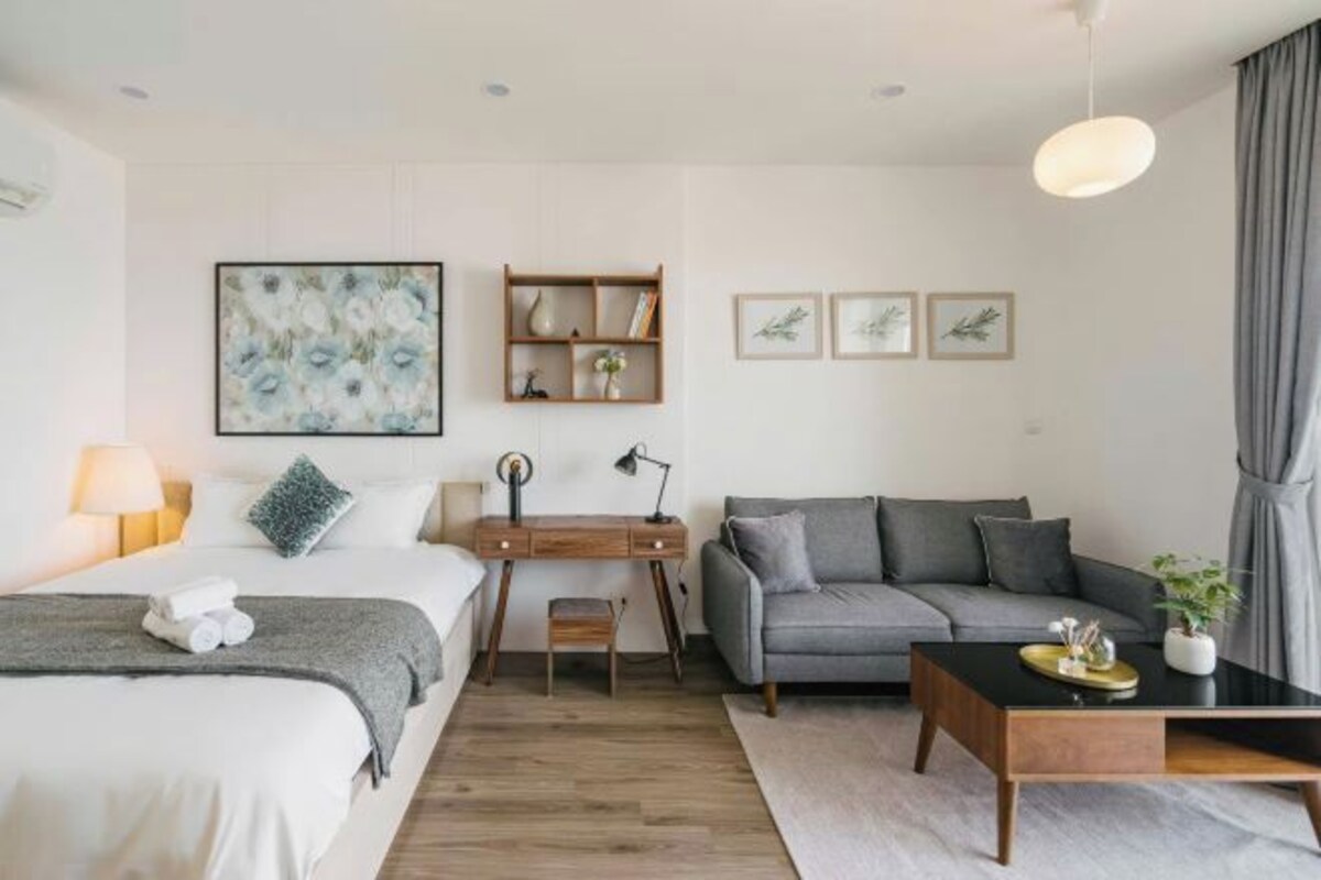 A modern hotel room with a bed, a desk, a sofa, and a coffee table.