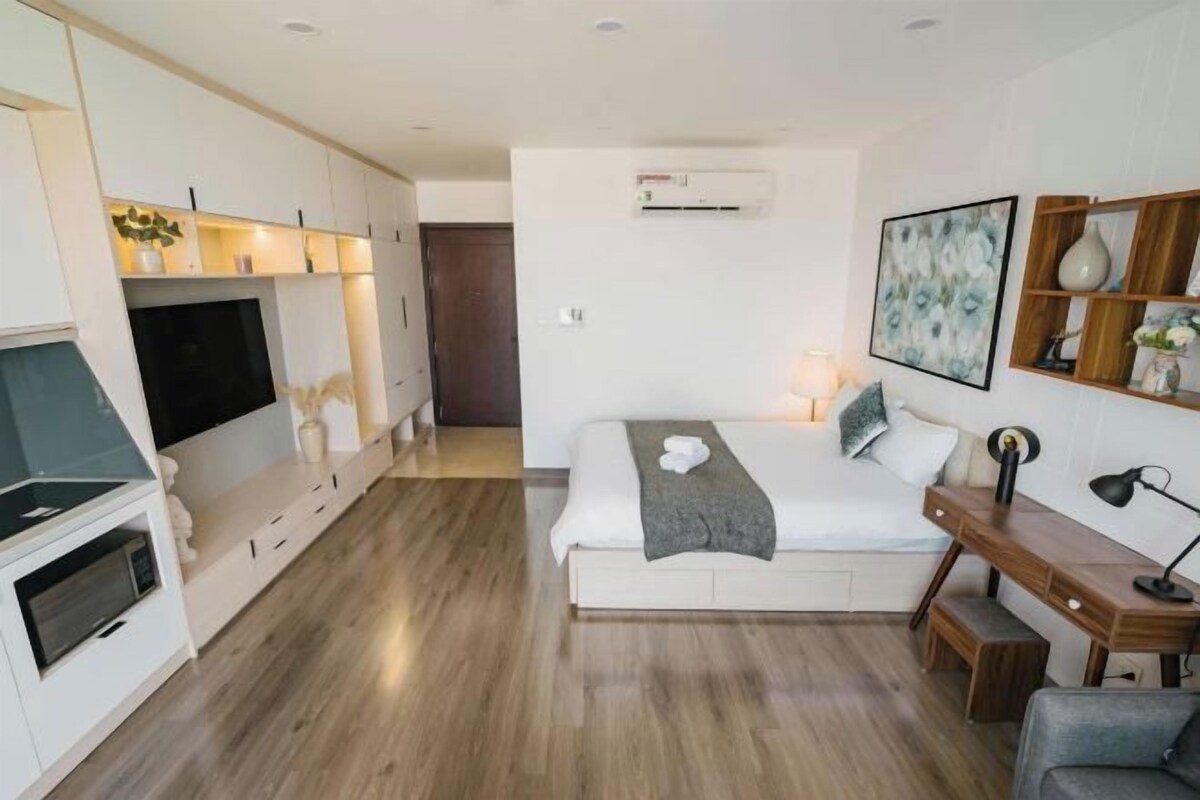 A modern hotel room with a bed, desk, and kitchenette.