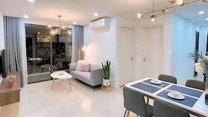 Een moderne woonkamer met een bank, eettafel en stoelen. Er staat een plant, een klein tafeltje met een vaas en een raam met gordijnen.