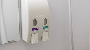 A wall-mounted dispenser with two buttons labeled "BODY SOAP" and "RINSE IN SHAMPOO".