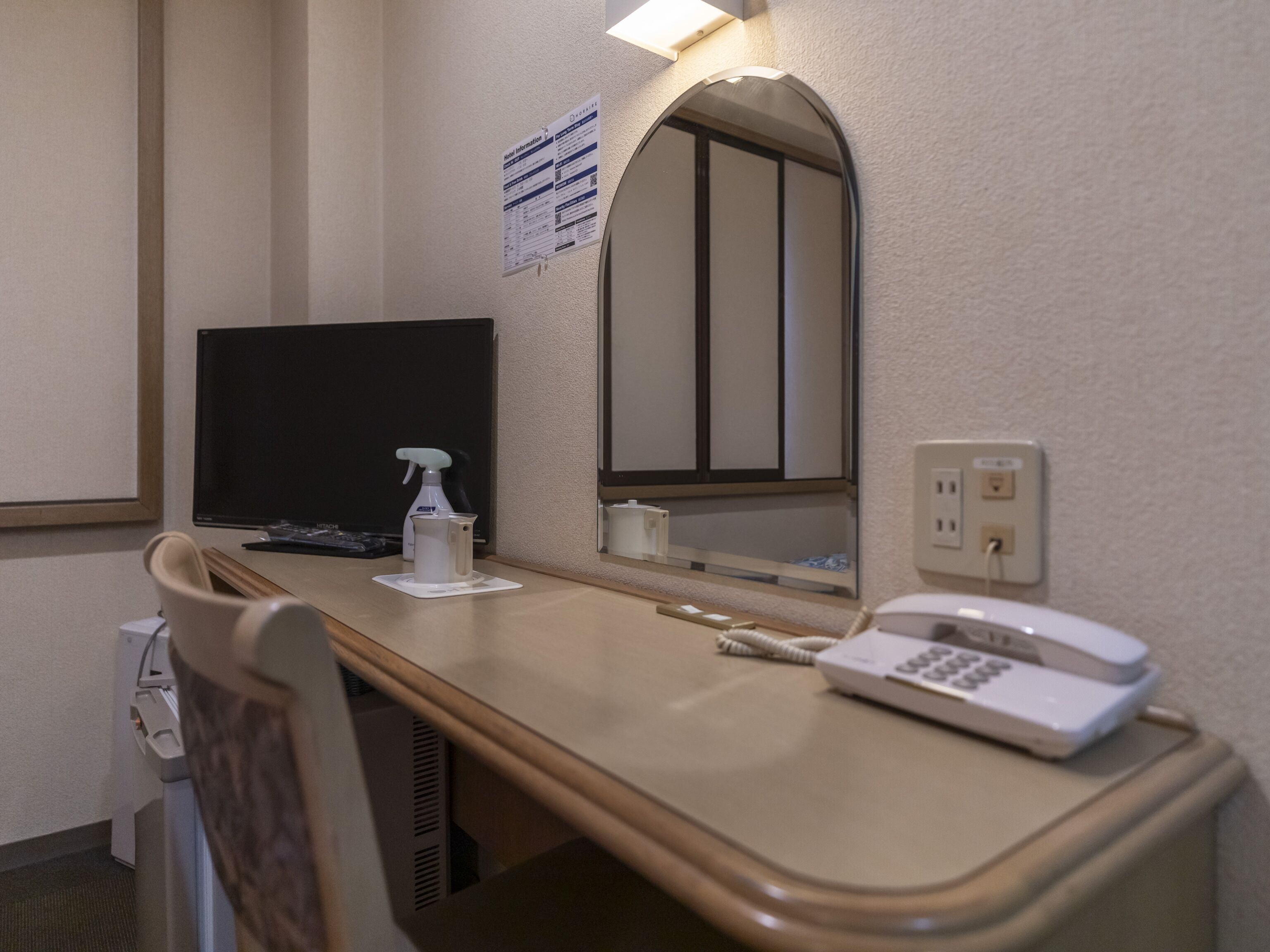 Een hotelkamer met een bureau, een spiegel, een telefoon, een spuitfles en een televisie.
