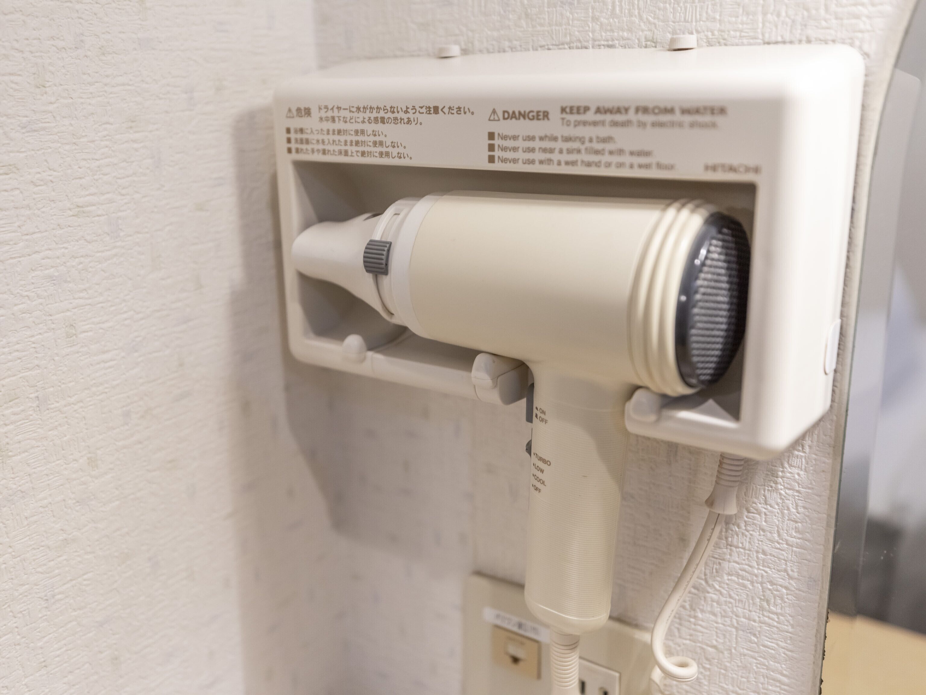 A hairdryer mounted on a wall with safety instructions and a power outlet below.