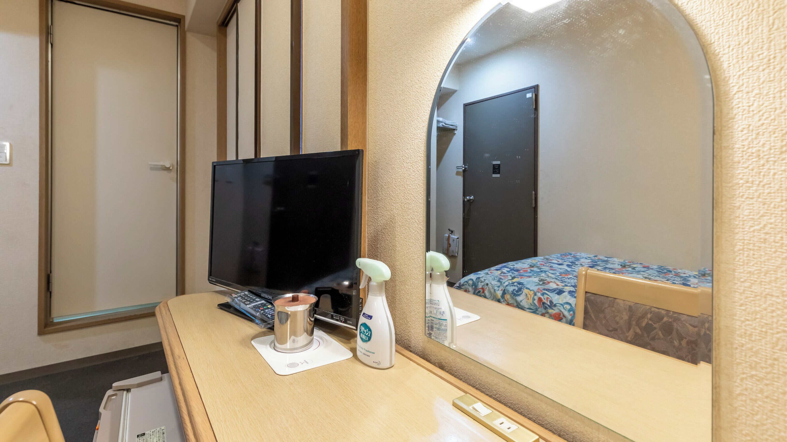 A hotel room with a TV, a desk with a computer, a mirror, a bed with a floral bedspread, and a door.