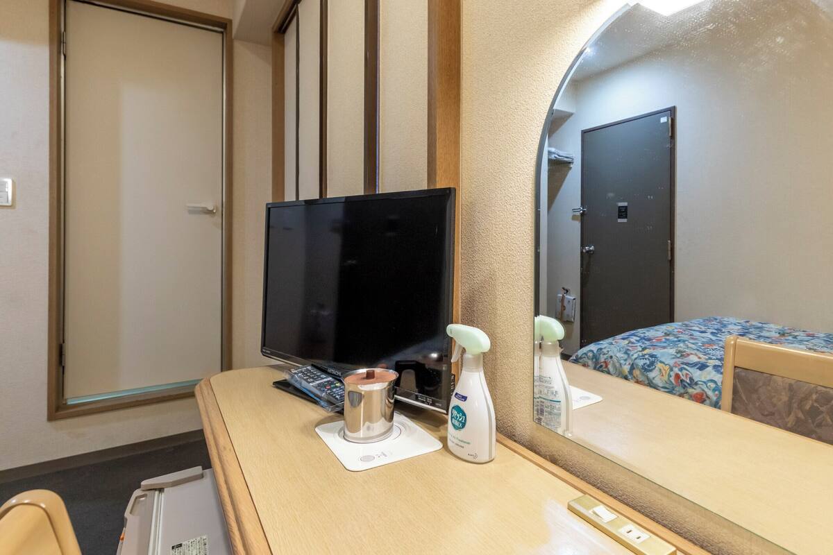 A hotel room with a TV, a desk with a computer, a mirror, a bed with a floral bedspread, and a door.