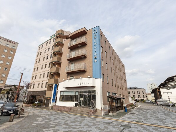 A multi-story hotel with a prominent blue sign, a ground-level entrance, and a visible parking area. - Hotel HORAIRE Saijo (Saijo)
