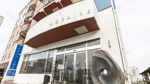 A hotel entrance with a modern facade, a large glass door, and a stone sculpture in front. - Hotel HORAIRE Saijo (Saijo)