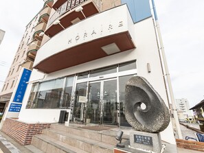 A hotel entrance with a modern facade, a large glass door, and a stone sculpture in front. - Hotel HORAIRE Saijo (Saijo)