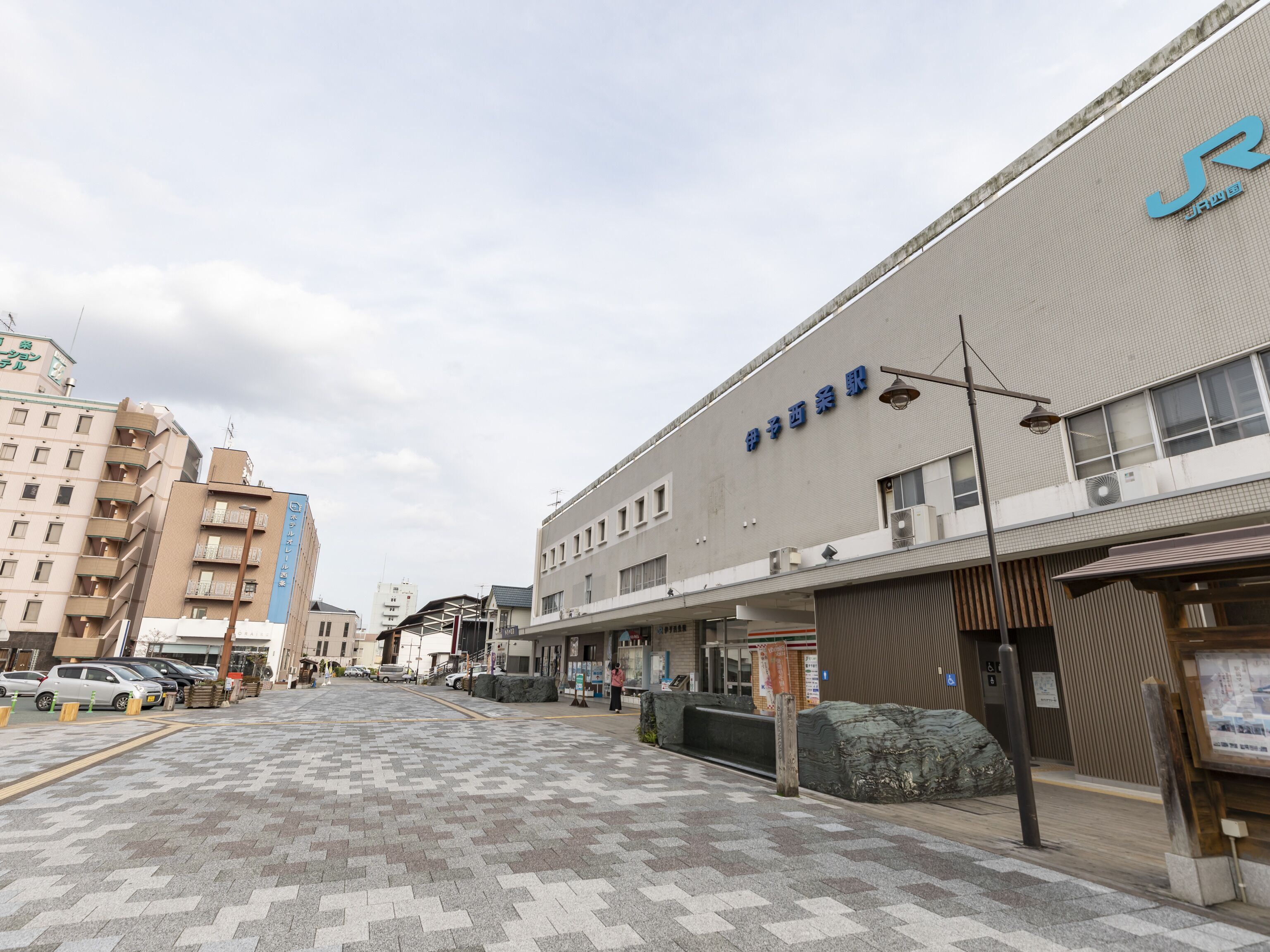A commercial building with a sign in Japanese characters, a paved walkway, and parked cars.
