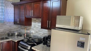 A kitchen with dark wooden cabinets, a stainless steel stove, a microwave, and a refrigerator. - 3 BDR Apt at Ramparts Near Sangster Airport (Montego Bay)