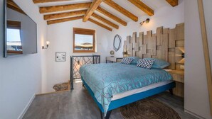 Ein Schlafzimmer mit einem Bett, Holzbalkendecke, Wand-Fernseher, einem Fenster und einem Spiegel.