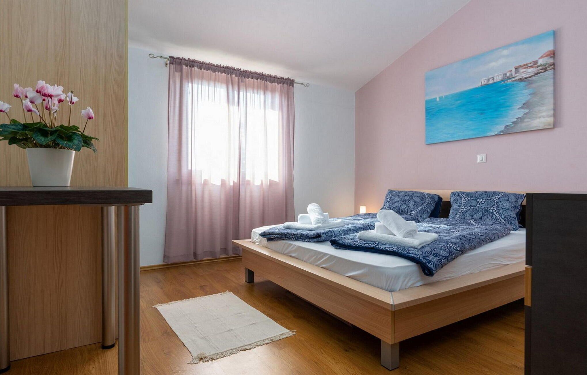 Une chambre à coucher avec un lit, une plante en pot, un tableau et une fenêtre avec des rideaux.