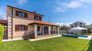 Una casa de dos pisos con balcón, piscina y césped bien cuidado.